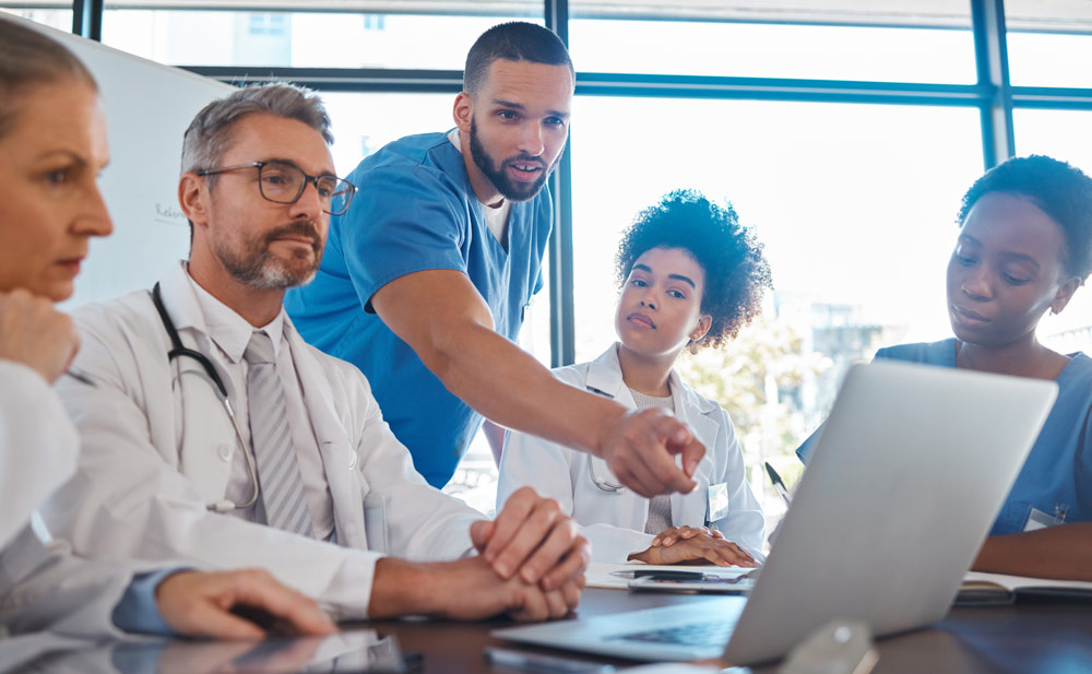 Medical professionals talking around table viewing laptop