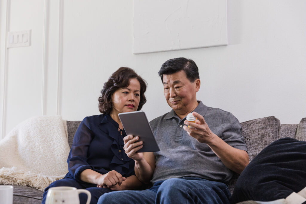 Senior man holding pill bottles video conferences with doctor