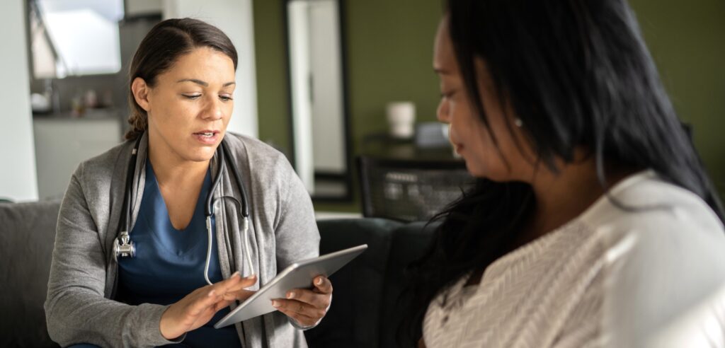 healthcare professional with stethoscope looks at mobile tablet while speaking an adult