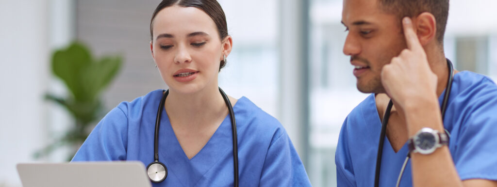 two healthcare professionals work at laptop together